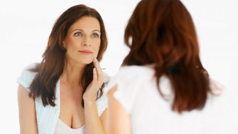 Woman checking skin in mirror mature 1024x576 996x560
